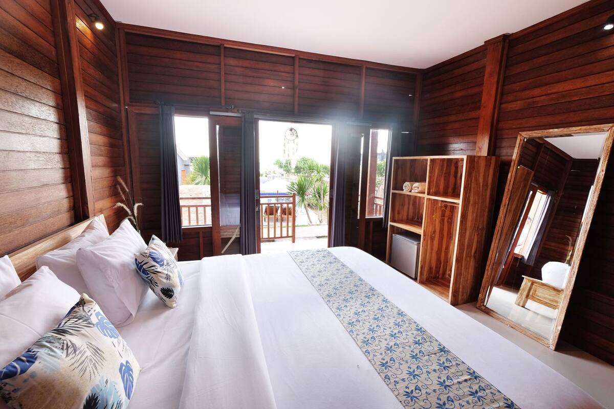 A wooden-paneled room with a bed, a wardrobe, and a balcony with a view.