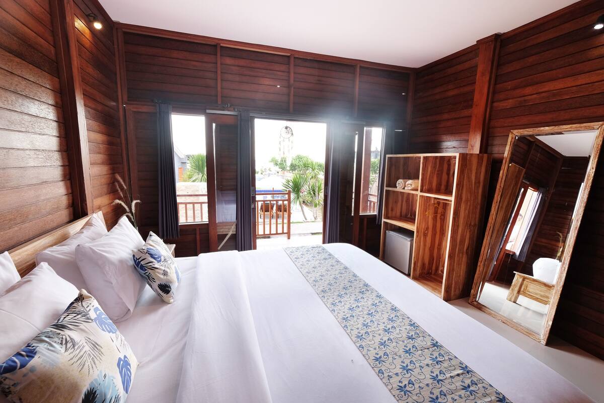 A bedroom with a large bed, wooden walls, a balcony with a table and chairs, and a mirror.