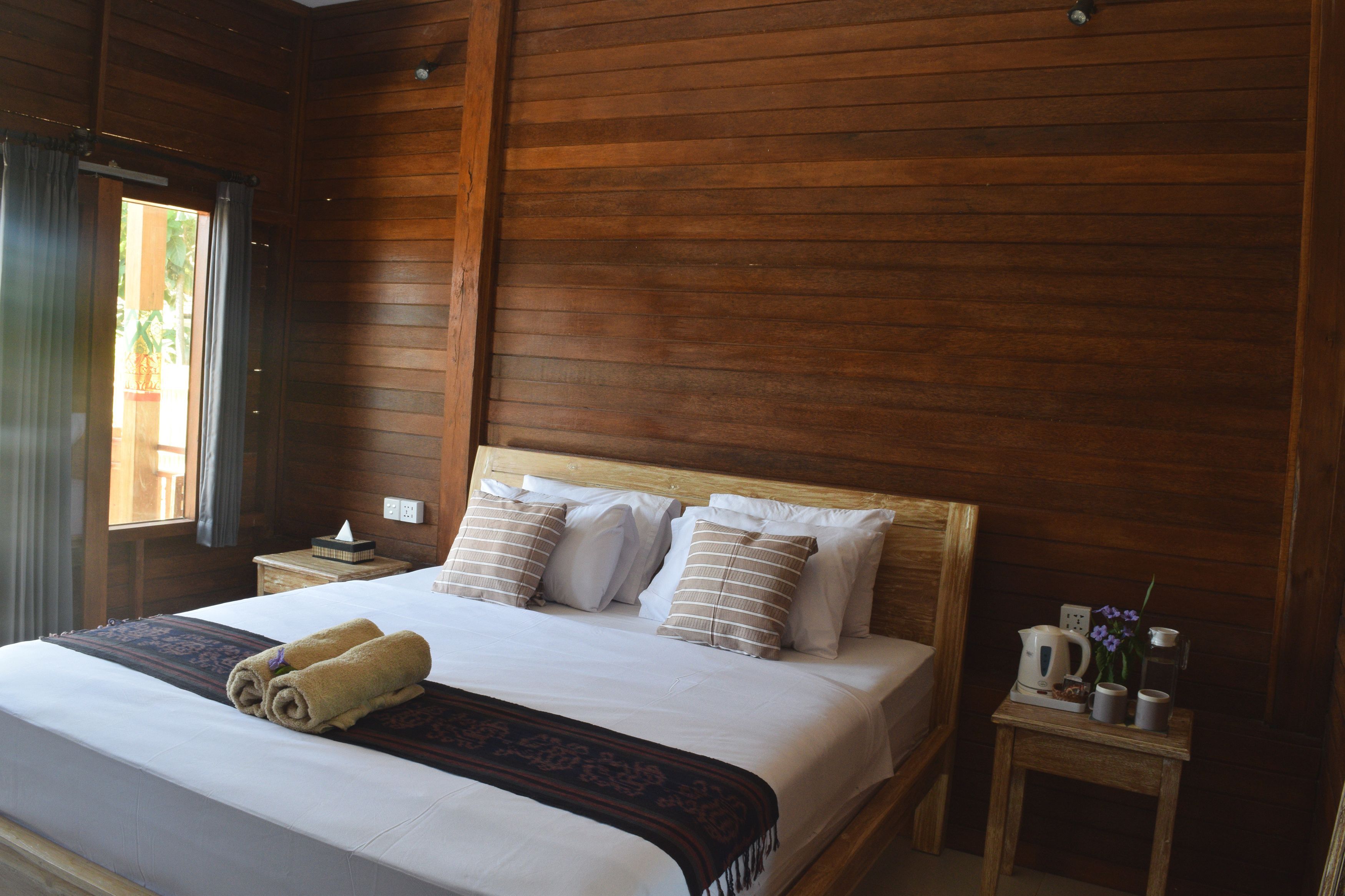 A neatly made bed with a wooden headboard, a bedside table with a lamp, and a window with curtains.