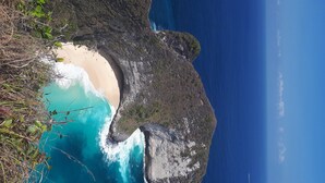 Paisagem costeira com uma rocha imponente, uma praia de areia e águas azuis cristalinas.