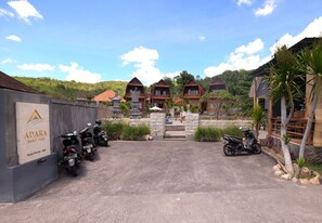 A gated entrance to a resort with multiple buildings, a sign for Adara Beach Huts, and several parked scooters.