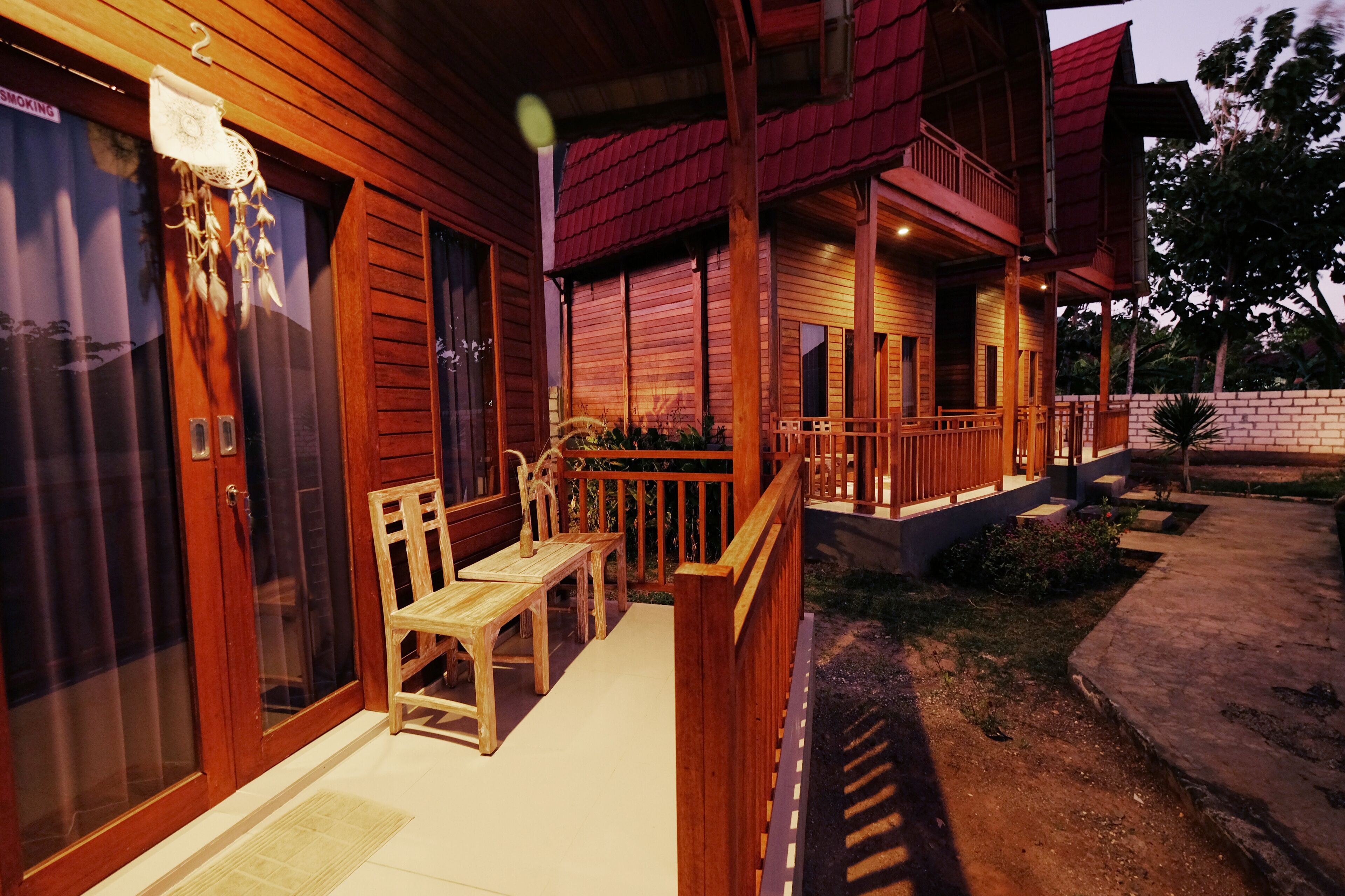 A wooden cabin with a porch, a dining area with chairs, and a small garden.