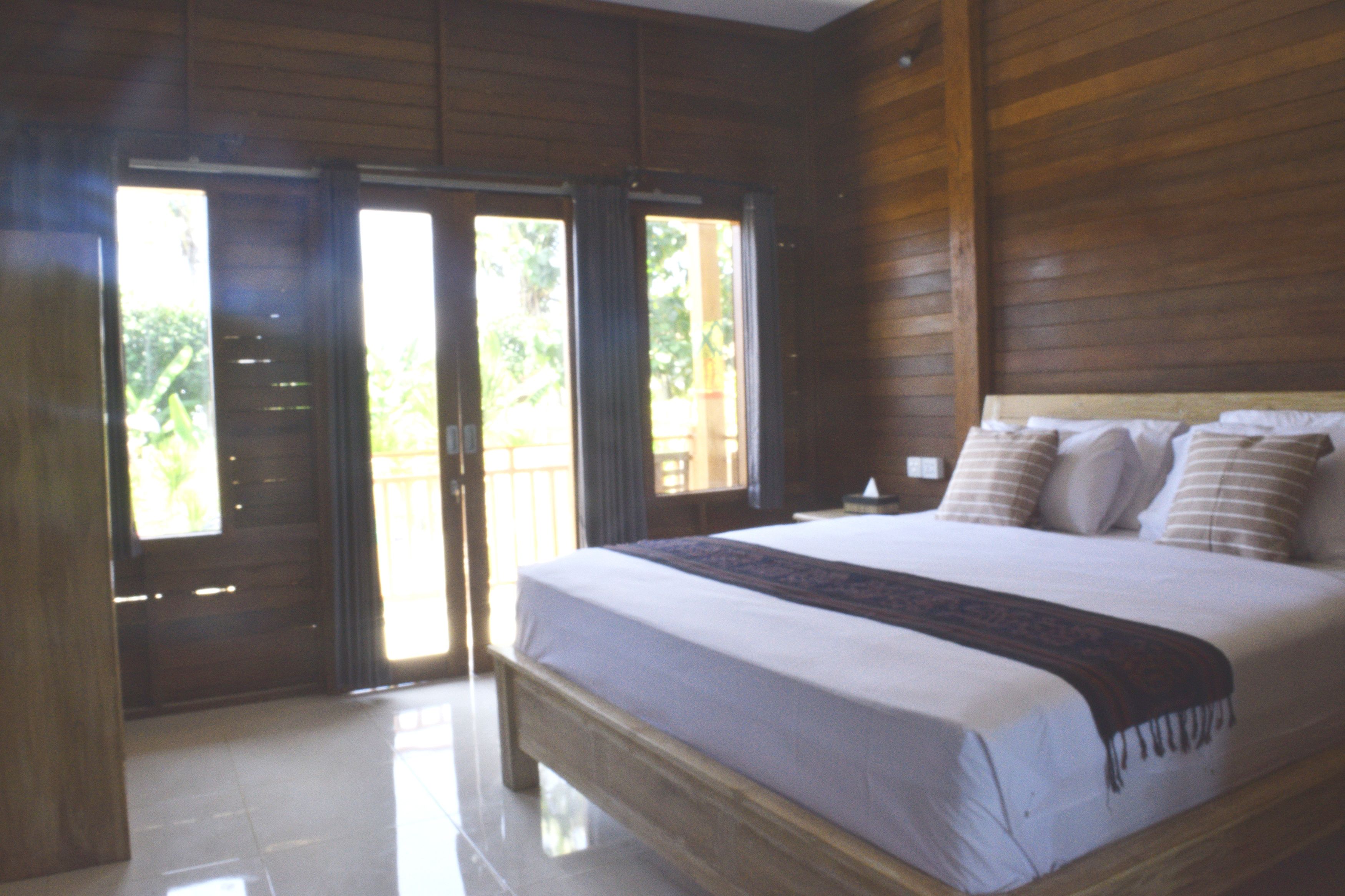 Een slaapkamer met een groot bed, houten wanden en uitzicht door de deur.