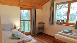 Una habitación acogedora con una cama grande, una cama más pequeña, una silla y una ventana con cortinas.