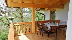 Una terraza de madera con una mesa dispuesta para dos, rodeada de sillas y una barandilla.