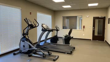 Un gimnasio con tres cintas de correr, un espejo grande y una puerta con un teléfono rojo de emergencia.