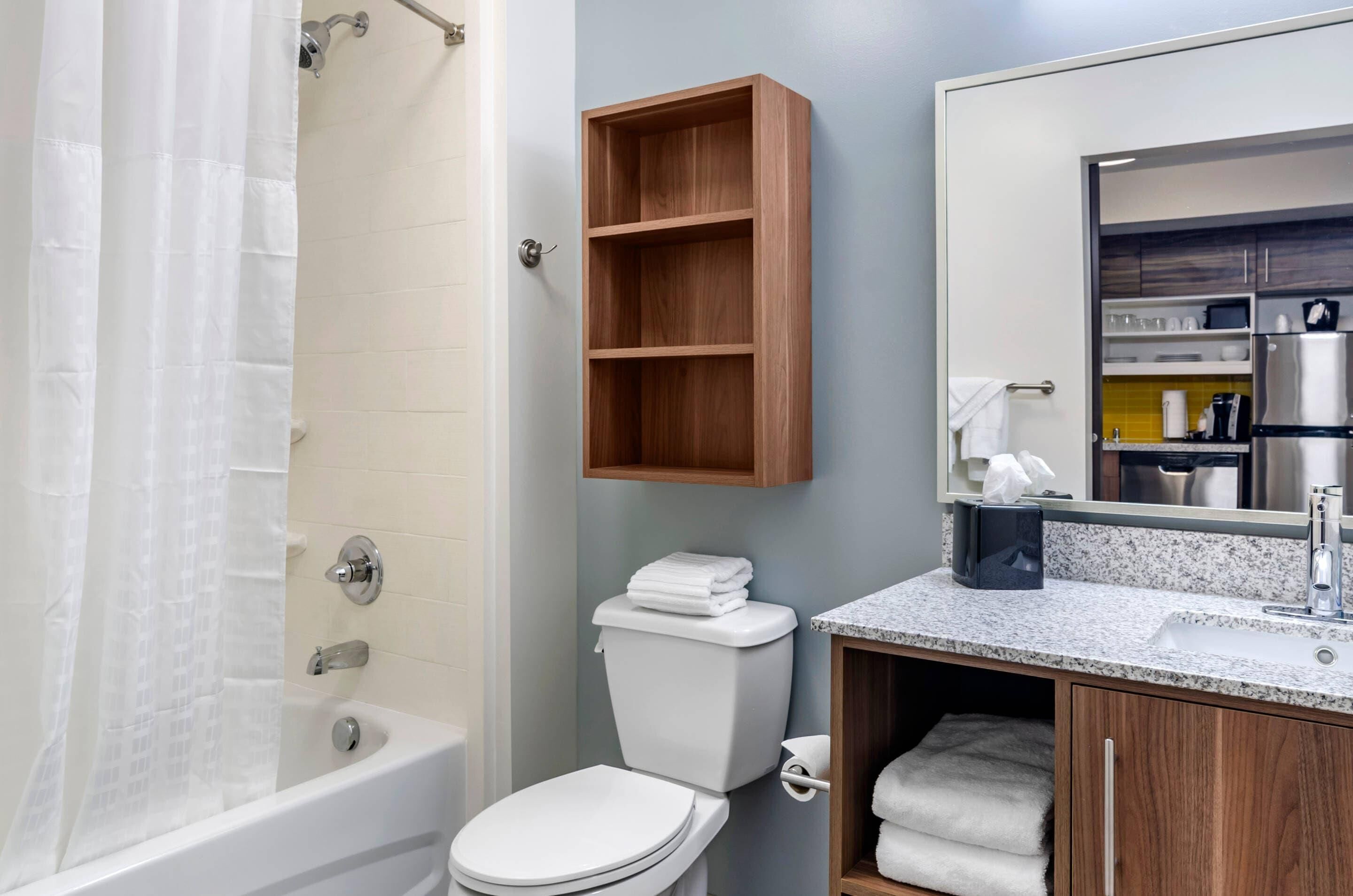 A bathroom with a bathtub, toilet, and a wooden shelf above the sink.