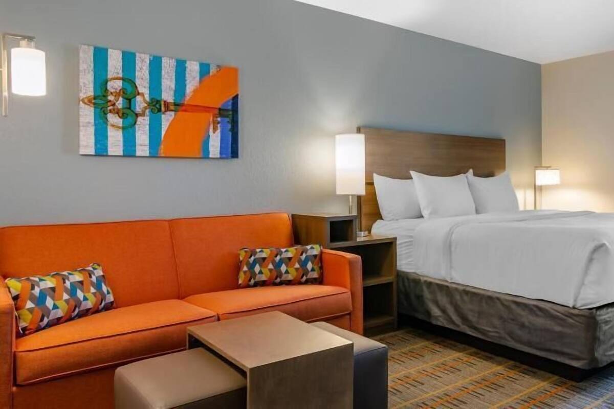 A hotel room with a bed, a sofa, a nightstand, a lamp, and a painting on the wall.