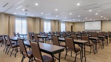 A conference room with multiple tables and chairs, a projector screen, and a carpeted floor.