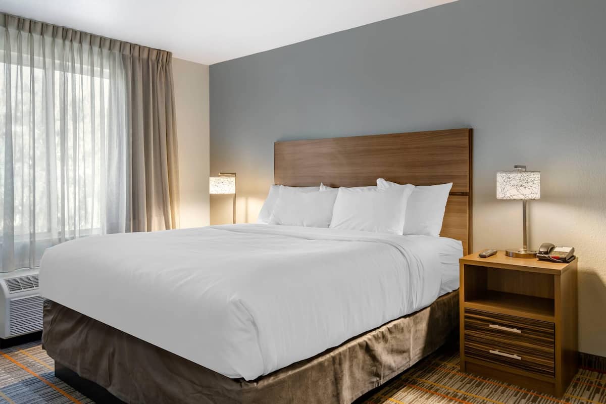 A hotel room with a large bed, bedside lamps, a nightstand, and a window with curtains.