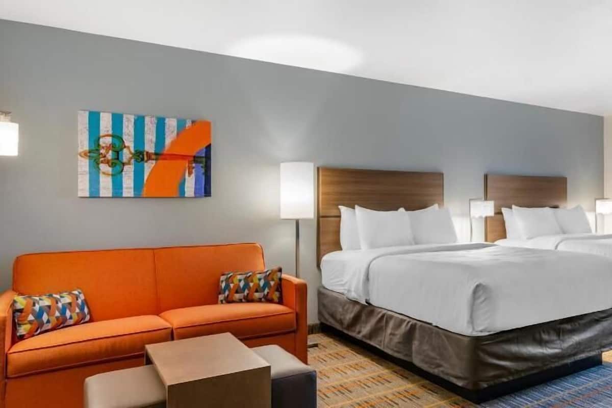 A hotel room with two beds, a sofa, a small table, and a colorful abstract painting on the wall.