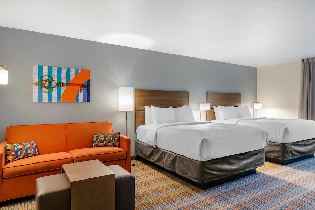 A hotel room with two beds, a sofa, a coffee table, and a painting on the wall.