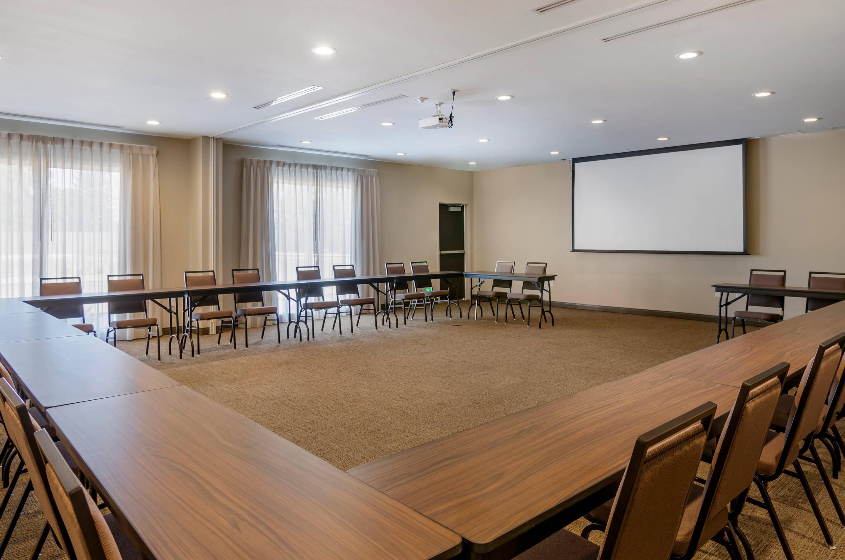 A conference room with a long table, chairs, a projector screen, and a carpeted floor.