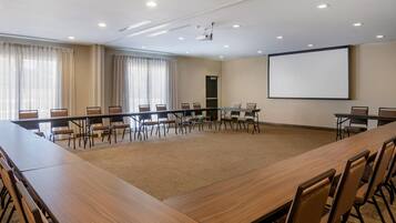 A conference room with a long table, chairs, a projector screen, and a carpeted floor.