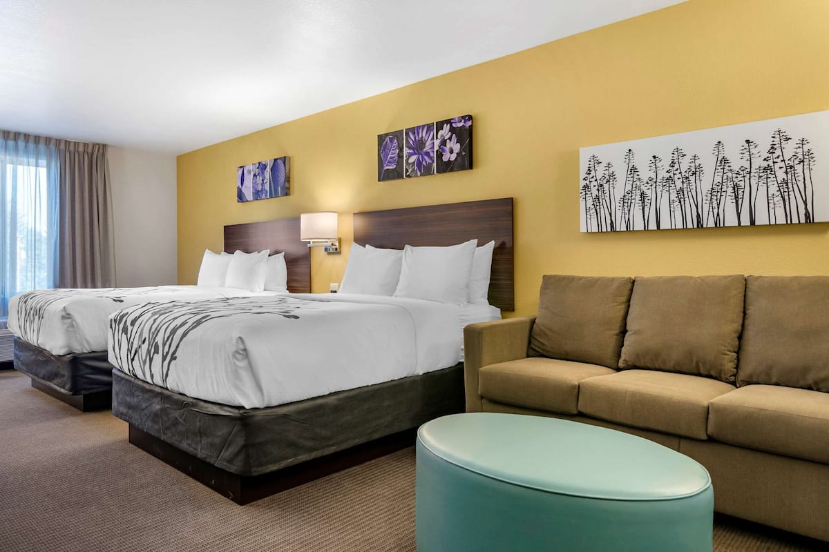 A hotel room with two beds, a sofa, and a small ottoman.