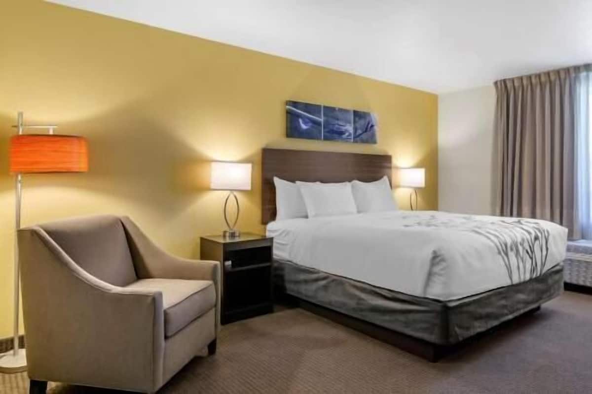 A hotel room with a bed, a chair, a nightstand, a lamp, and a painting on the wall.