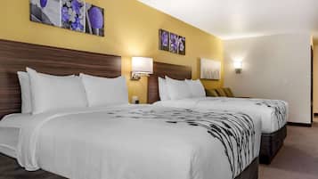 Hotelkamer met twee bedden, elk voorzien van witte beddengoed en een zwart bloemenmotief. Er hangen wandlampen en er is kunst te zien met bloemen.