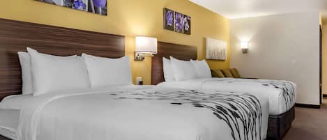 Quarto de hotel com duas camas, cada uma com roupa de cama branca e um padrão floral preto. Há luminárias fixadas na parede e obras de arte com flores.