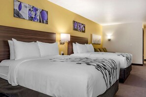 A hotel room with two beds, each with white bedding and a black floral pattern. There are wall-mounted lamps and artwork depicting flowers.