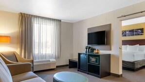 A hotel room with a sofa, a small table, a TV, a minibar, and a bed. - Sleep Inn Great Falls Airport (Great Falls)