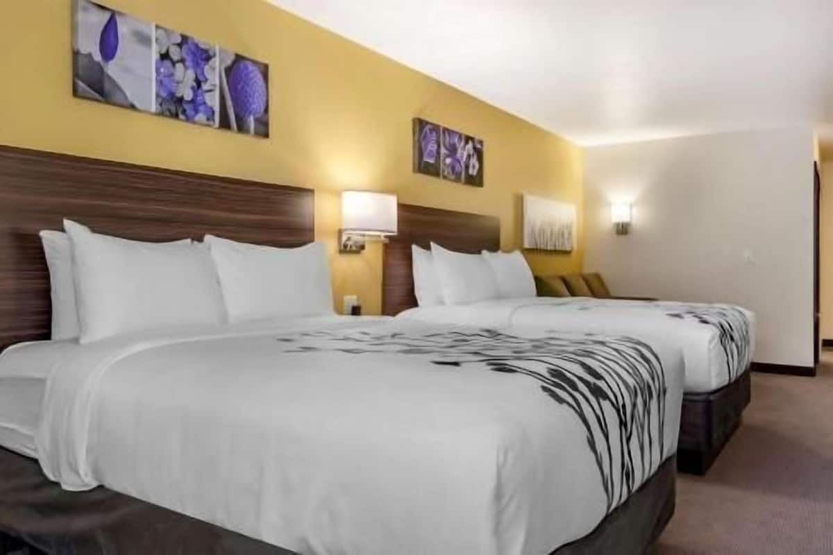 A hotel room with two beds, a wooden headboard, wall-mounted lamps, and artwork.