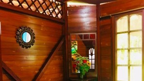 Una habitación tipo cabaña de madera con una cama, un espejo y una ventana que da a zonas verdes.