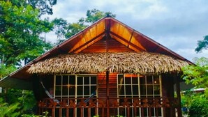 Una casa de madera con techo de paja, rodeada de abundante vegetación.