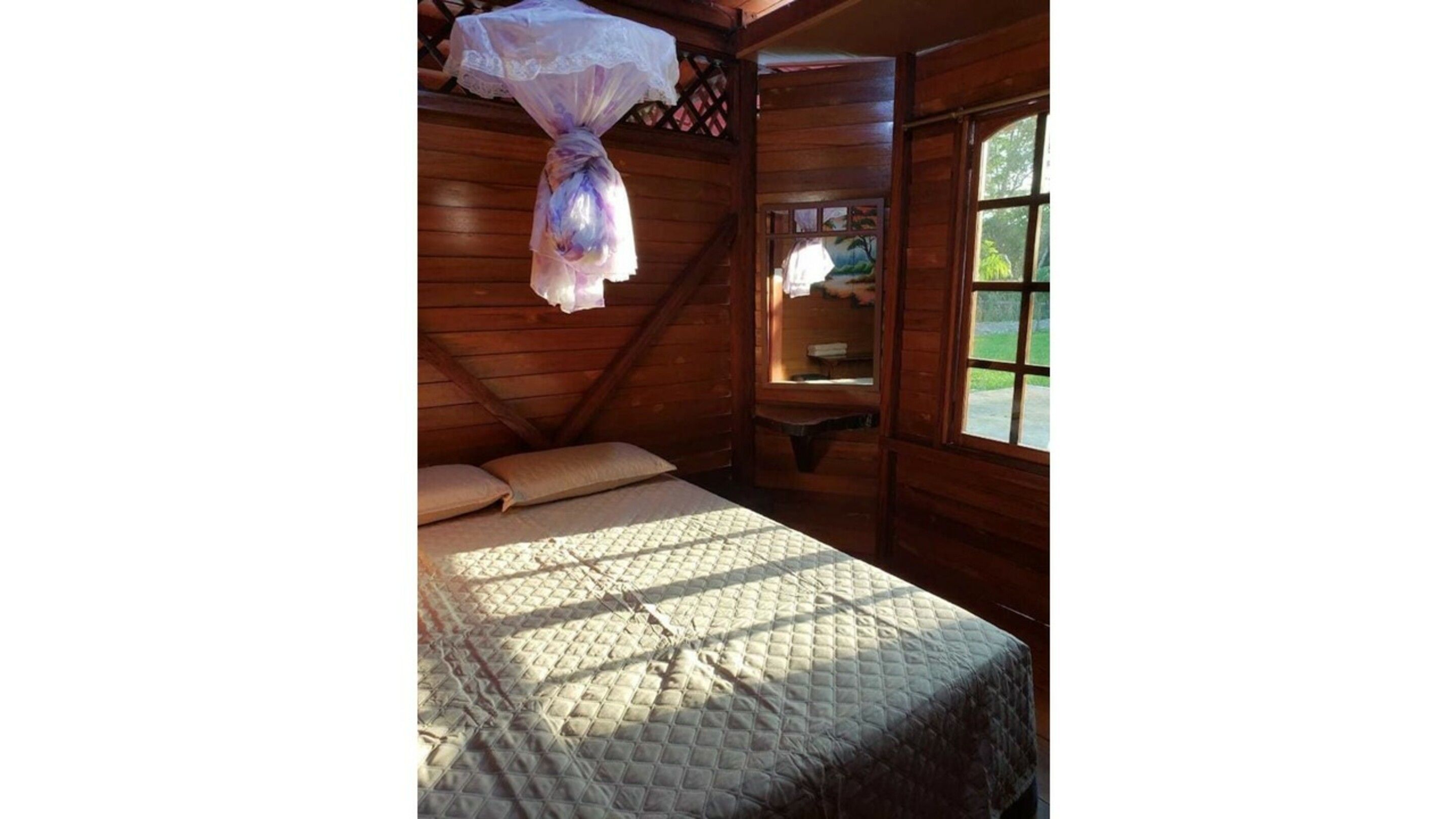 Una habitación de madera con cama, almohadas y mosquitera.