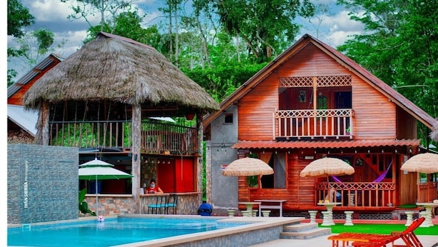 Una casa de madera con techo de paja, piscina y mobiliario de exterior.
