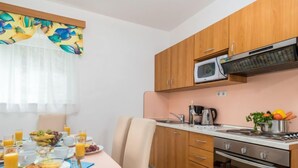 A compact kitchen with wooden cabinets, a microwave, a stove, and a dining area with breakfast set.