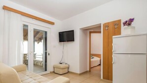 A modern living room with a sofa, a television, a refrigerator, and a sliding door leading to a balcony.
