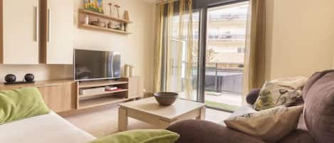 A modern living room with a sofa, a TV, a coffee table, and a balcony with curtains.
