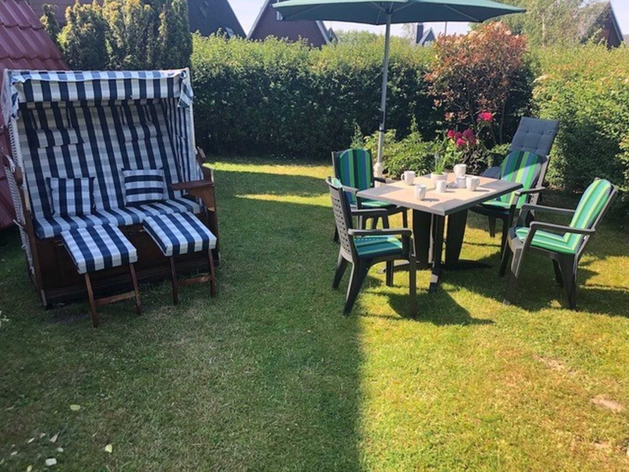 En terrasse med en stribet liggestol, et bord med stole og en parasol.