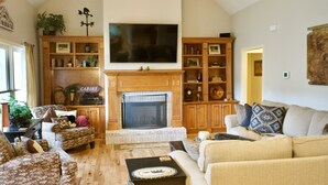 A cozy living room with a fireplace, wooden cabinets, and a flat-screen TV mounted above it. - Explore, Relax: Mountain House, Yahoola Creek, Cherokee Forest (Dahlonega)