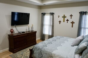 A bedroom with a bed, dresser, TV, and wall-mounted crosses.
