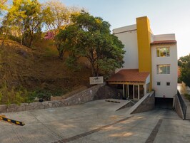 Un edificio con fachada amarilla, un muro de contención de piedra y una zona de entrada cubierta.
