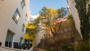 Un patio con una escalera, un parterre de flores y un edificio de múltiples ventanales y pared amarilla.