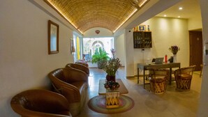 Un hall de hotel con techo alto, una zona de estar con sillones de cuero, una mesa de comedor con sillas y una planta en maceta.