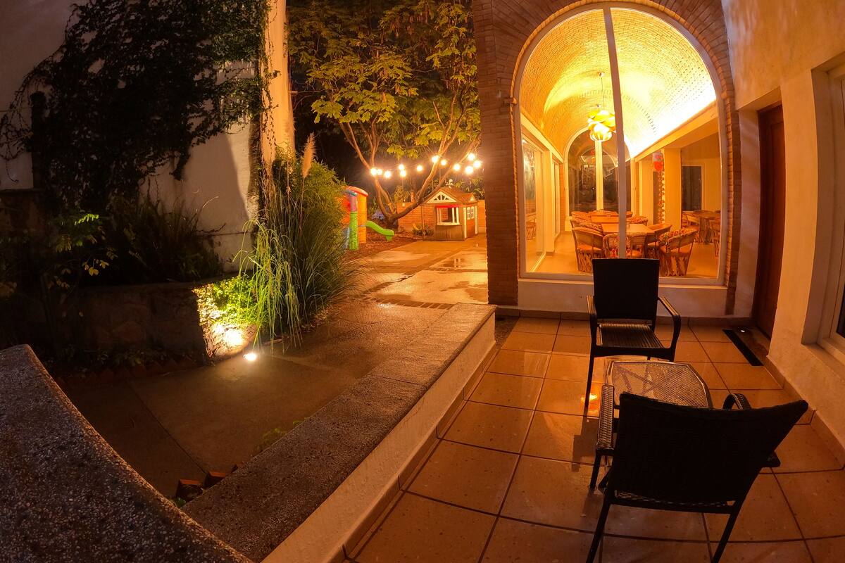 Un patio con mesa y sillas, un pequeño espacio de juegos y un edificio con entrada curva.