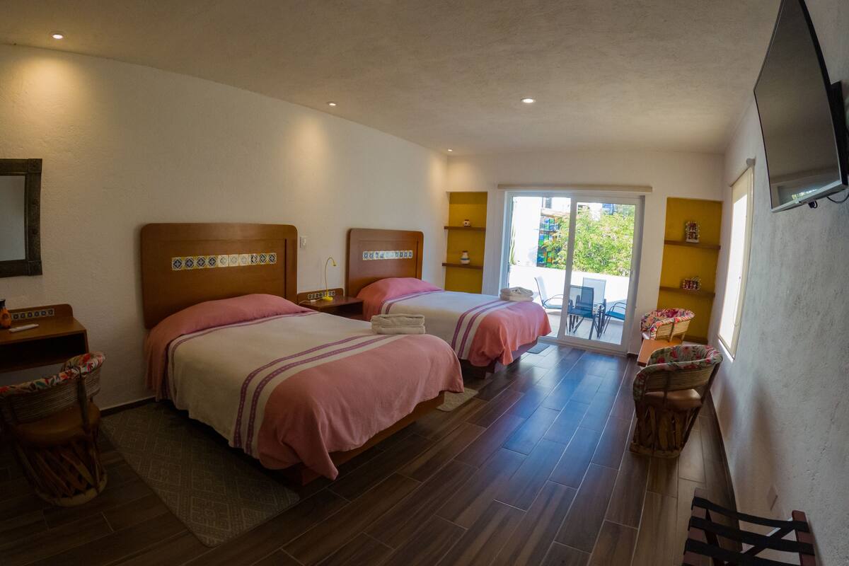 Habitación de hotel con dos camas, televisión, balcón y piso de madera.