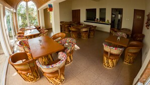 Un comedor amplio con múltiples mesas y sillas de madera, ventanas grandes que proporcionan luz natural y vistas al exterior.