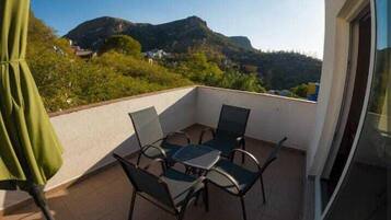 Uma varanda com mesa e cadeiras, um guarda-sol verde e vista para montanhas.