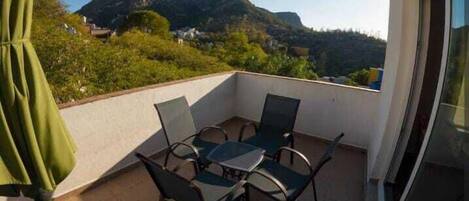 A balcony with a table and chairs, a green umbrella, and a view of mountains.