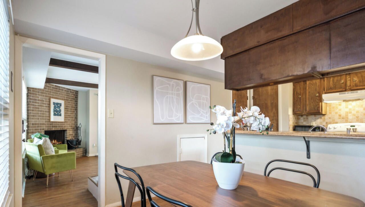A dining area with a wooden table, chairs, a potted orchid, and a hanging light fixture.