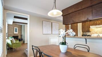 A dining area with a wooden table, chairs, a potted orchid, and a hanging light fixture.