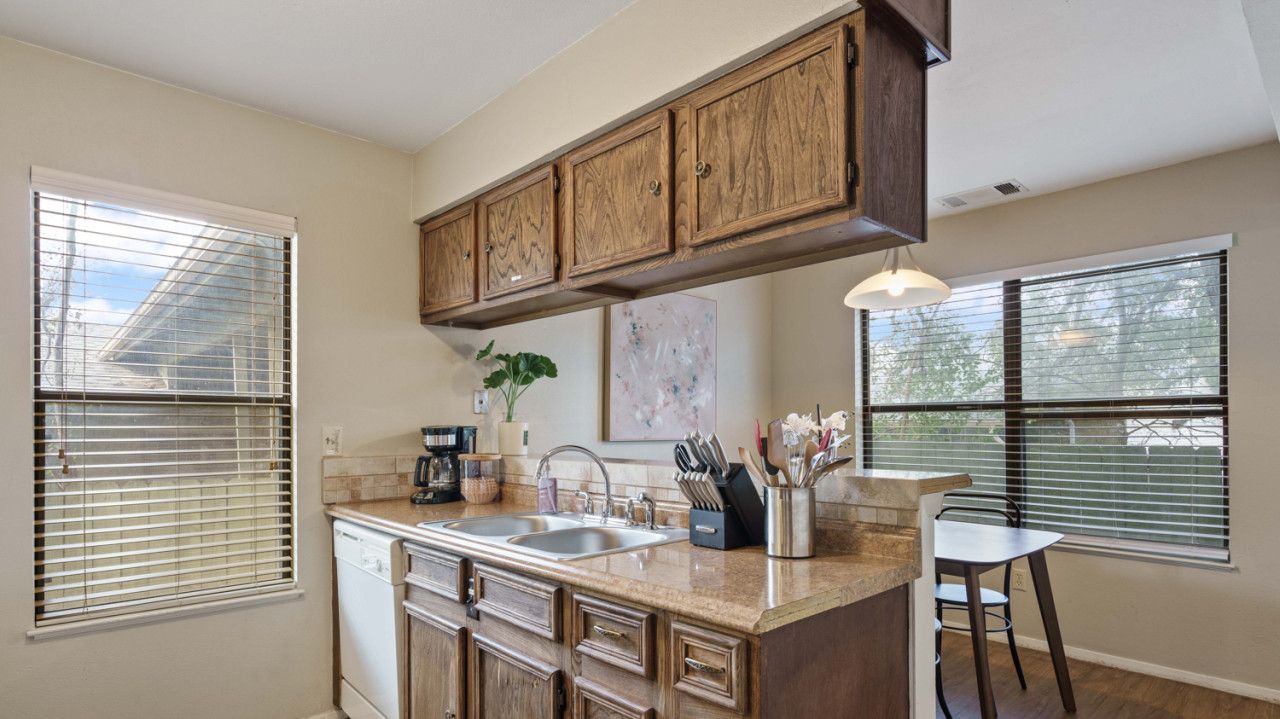 A kitchen with wooden cabinets, a dishwasher, a sink, and a dining area with a table and chairs.