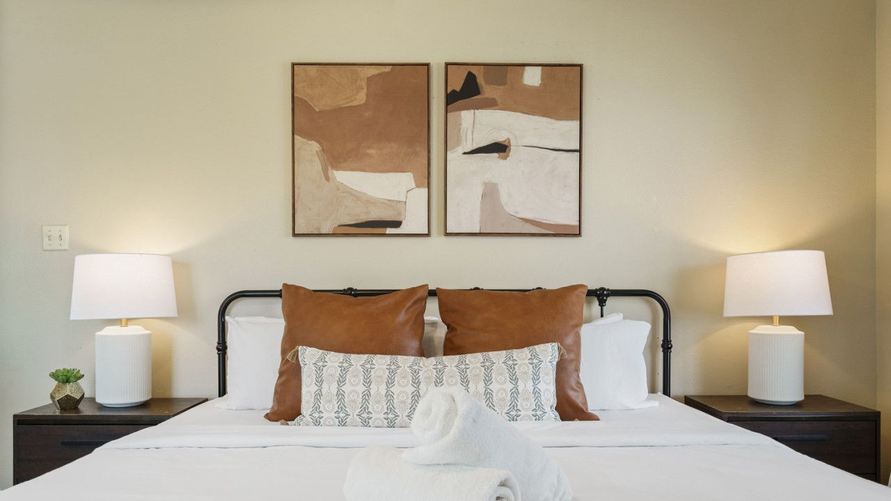 A hotel room with a bed, two nightstands, two lamps, and two abstract paintings on the wall.