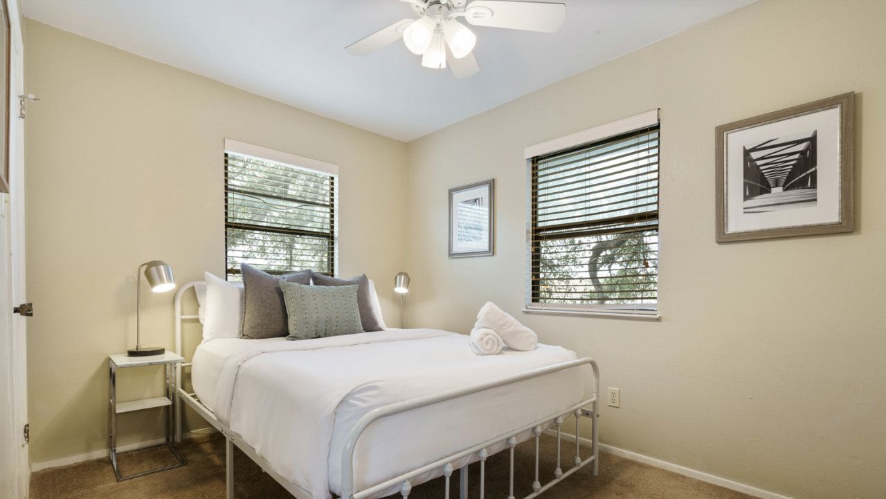 A bedroom with a bed, bedside tables, a ceiling fan, and windows with blinds.
