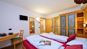 Une chambre d’hôtel avec deux lits, un bureau avec une chaise, une télévision, un miroir et une armoire.