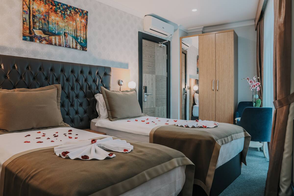 A hotel room with two beds, a large painting, an air conditioning unit, and a mirror.